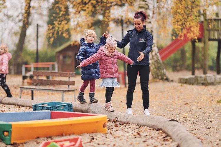 Erzieherin unterstützt Kinder beim balancieren.