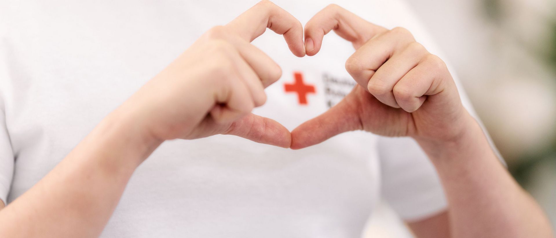 Zwei Hände formen ein Herz und welche das Logo des DRK einrahmen.