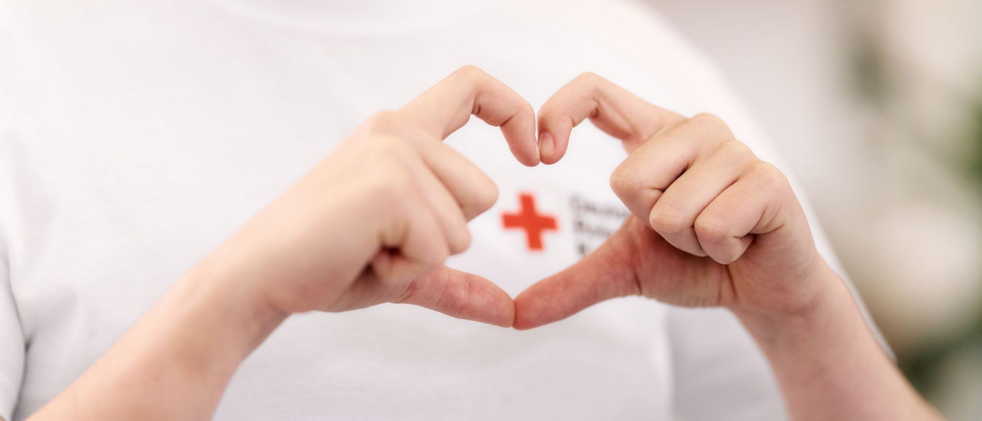 Zwei Hände formen ein Herz und umkreisen damit das Rote Kreuz.
