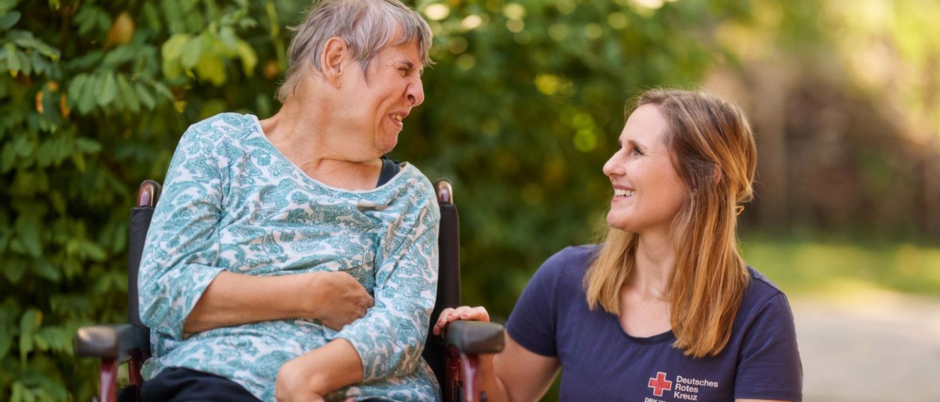 Mitarbeiterin des DRK lächelt sich an mit Nutzerin mit Teilhabeeinschränkung.