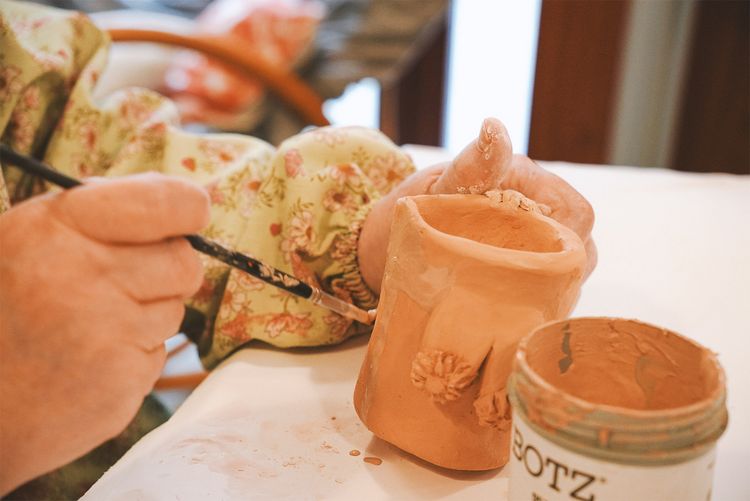 Hände eines Nutzers bemalen ein getöpfertes Werk.