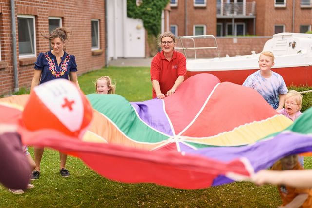 Erzieher und Kinder schwingen ein großes buntes Tuch.