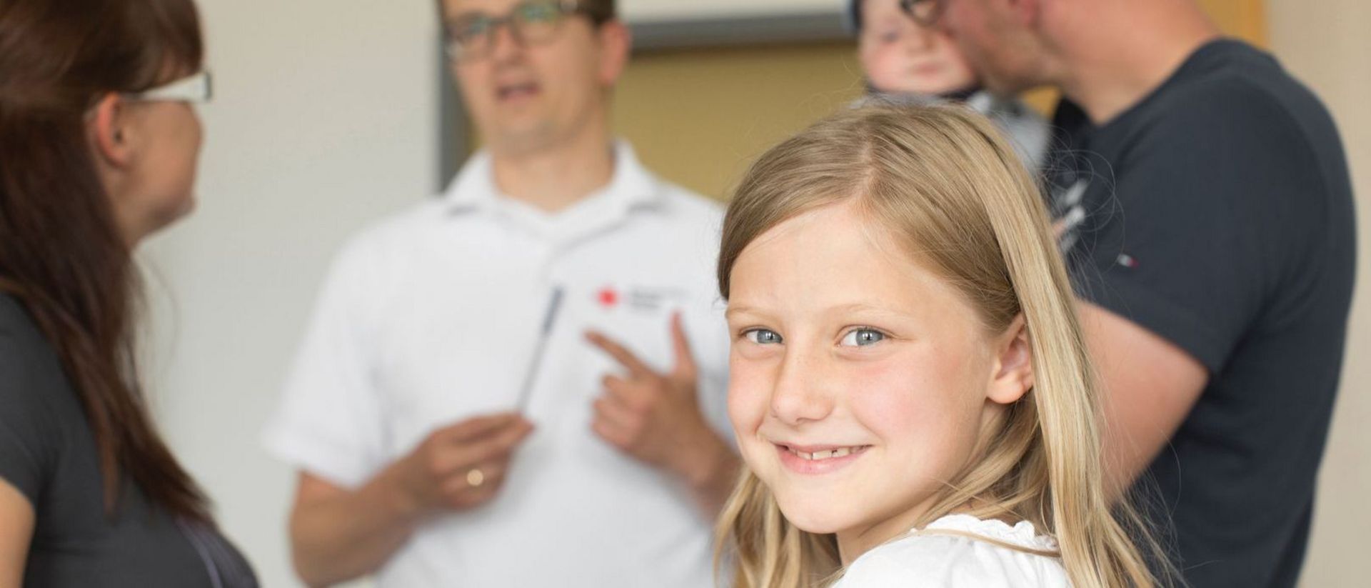 DRK-Mitarbeiter berät Familie und Kind lächelt in die Kamera.