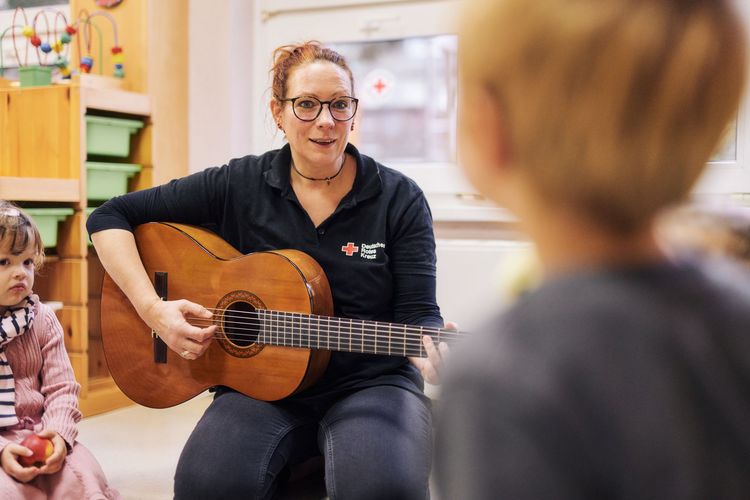 Erzieherin spielt Gitarre und Kinder hören zu.