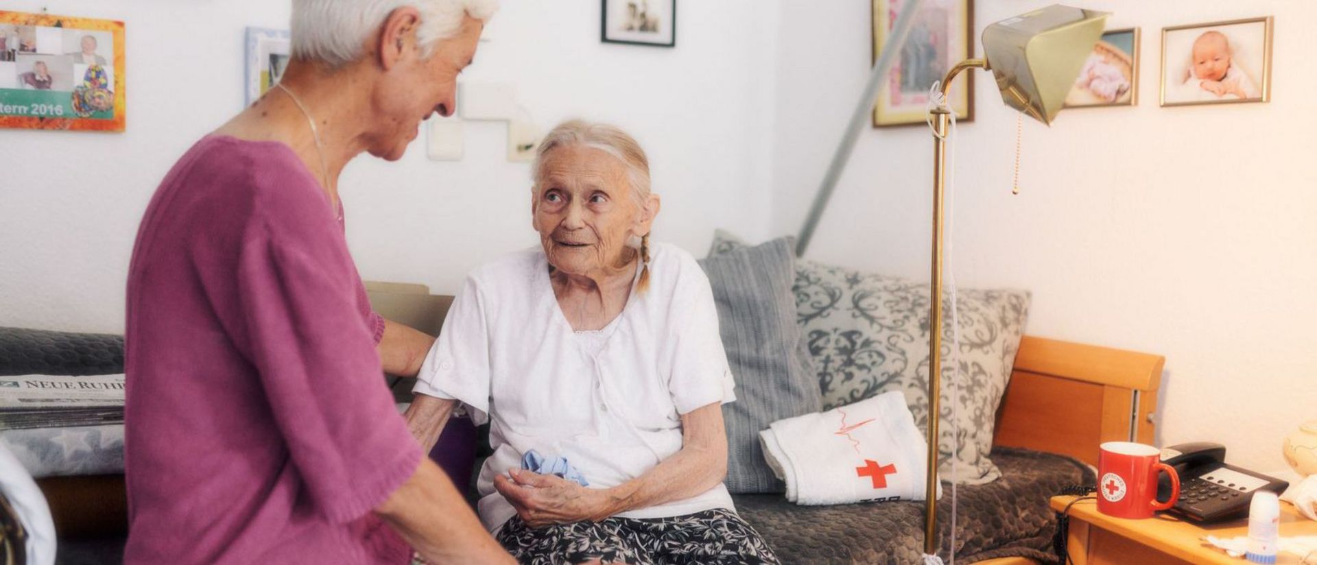 Mitarbeiterin des DRK sitzt mit Seniorin am Bett im Gespräch.