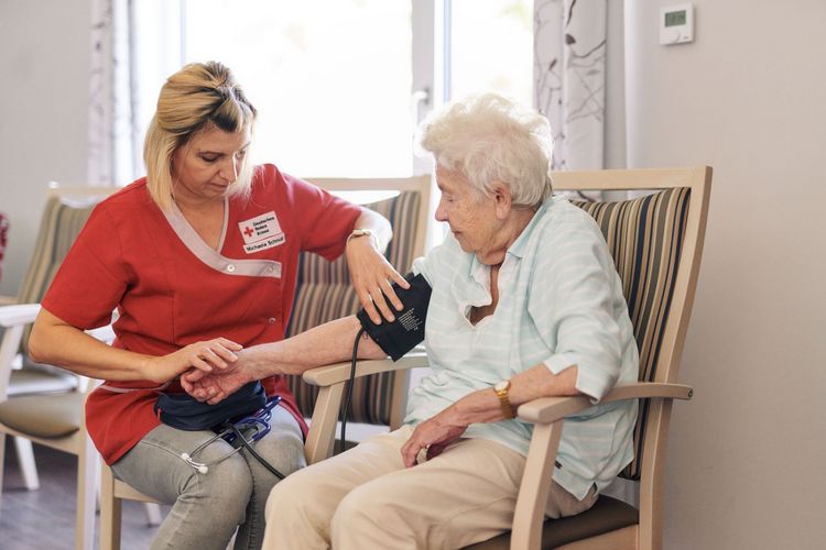 DRK Mitarbeiterin misst Blutdruck bei Seniorin.
