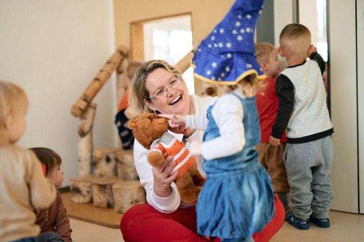 Erzieherin übergibt verkleidetem Kind ein Kuscheltier.